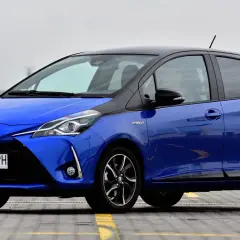 Niebieska Toyota Yaris Hybrid, z czarnym dachem, zaparkowana na zewnątrz. Ile koni ma Toyota Yaris? Ten model ma 100 KM.