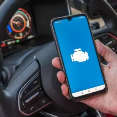 Dacia Sandero z ikoną silnika na ekranie telefonu, gotowa do diagnostyki OBD.