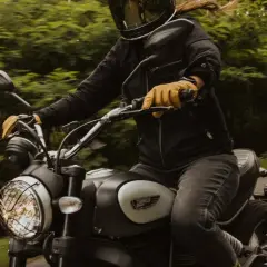 Motocyklista w kasku i rękawiczkach jedzie motocyklem. W tle zielony las. To świetny moment, by nauczyć się, jak zmieniać biegi w motorze.