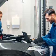 Mechanicy diagnozują drgania samochodu podczas przyspieszania. Jeden sprawdza silnik latarką, drugi analizuje dane na laptopie.