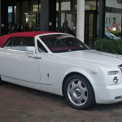 Biały Rolls-Royce Phantom Drophead Coupe z czerwoną, opuszczoną dachem, zaparkowany przed budynkiem.