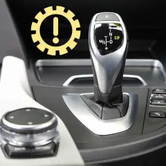 Awaryjne odblokowanie skrzyni biegów w BMW. Ikona ostrzeżenia nad dźwignią zmiany biegów.