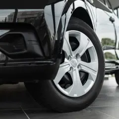 Zbliżenie na przednie koło czarnego Dacia Duster z oponami letnimi. Felga aluminiowa z logo marki.
