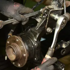 Mechanik w rękawiczkach dokonuje wymiany łożyska w kole tylnym, używając kluczy do odkręcenia śrub mocujących.