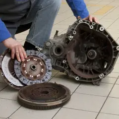 Mechanik pokazuje rozłożony element sprzęgła, w tym koło zamachowe i tarczę, gotowe do wymiany łożyska wałka sprzęgłowego.