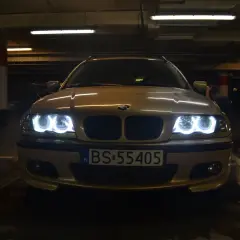 Złote BMW E46 z włączonymi ringami świeci w ciemnym garażu.