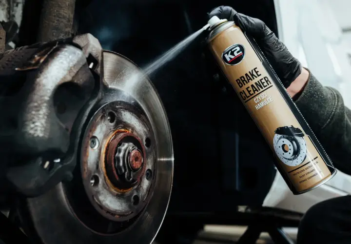 Ręka w czarnej rękawiczce rozpyla środek K2 Brake Cleaner na zużyte tarcze hamulcowe, usuwając rdzę i brud z ich rantów.