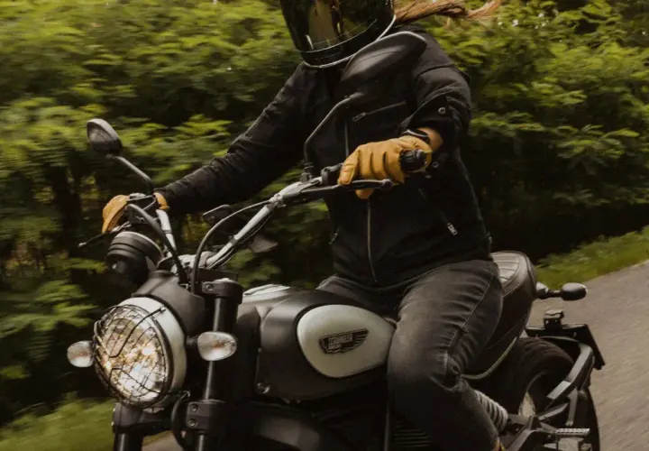 Motocyklista w kasku i rękawiczkach jedzie motocyklem. W tle zielony las. To świetny moment, by nauczyć się, jak zmieniać biegi w motorze.
