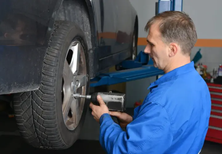 Mechanik w niebieskim kombinezonie dokręca śruby koła. To ważny moment dokręcania docisku sprzęgła LUK.