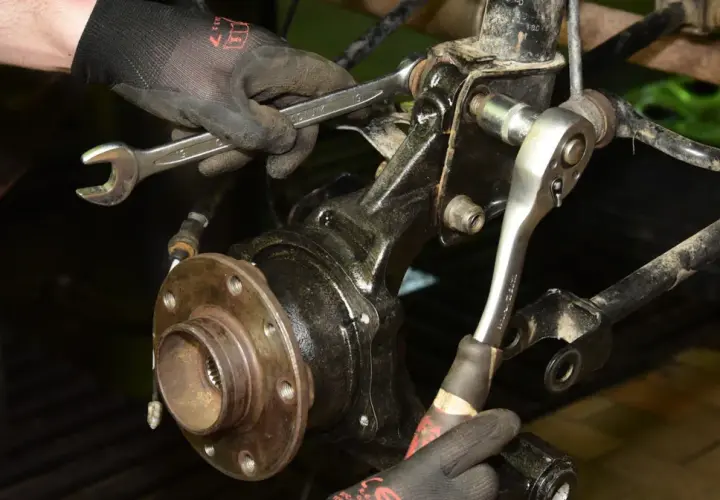 Mechanik w rękawiczkach dokonuje wymiany łożyska w kole tylnym, używając kluczy do odkręcenia śrub mocujących.