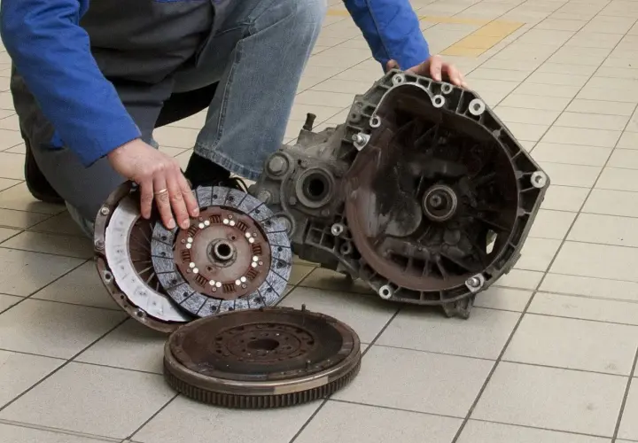 Mechanik pokazuje rozłożony element sprzęgła, w tym koło zamachowe i tarczę, gotowe do wymiany łożyska wałka sprzęgłowego.