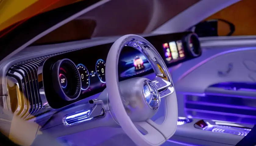 Wnętrze Mercedesa CLA z futurystycznym kokpitem, podświetlanym na niebiesko. Widoczny ekran, kierownica i cyfrowe zegary.