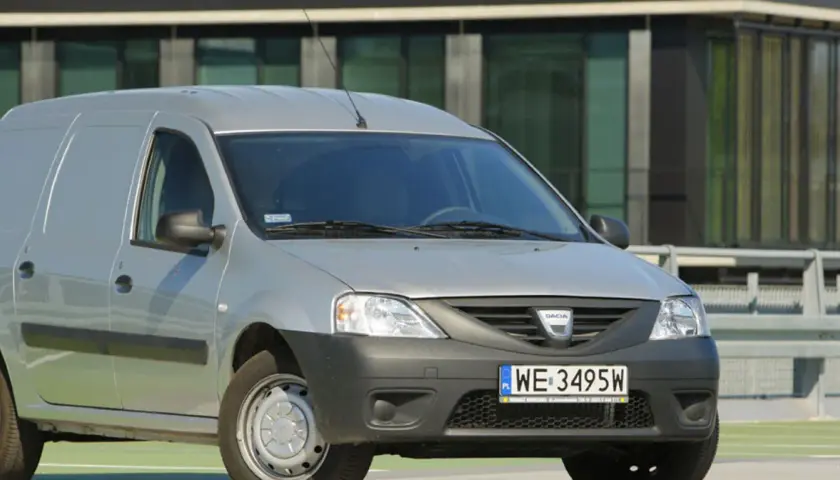 Srebrny Dacia Logan Van z polskimi tablicami WE 3495W zaparkowany przed nowoczesnym budynkiem.