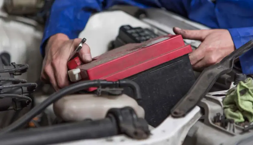 Mechanik wymienia akumulator BMW E46. Czerwona pokrywa akumulatora jest widoczna.