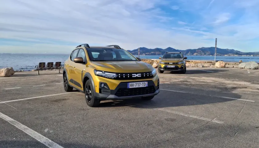 Dwa złote Dacia Sandero Stepway na tle morza i gór. Dwa modele, różne silniki, gotowe na przygodę.