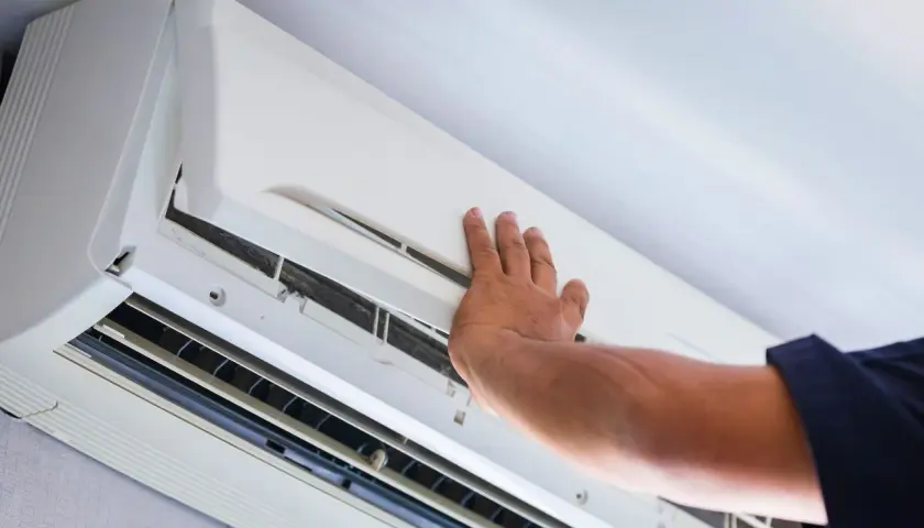 Ręka sprawdza stan klimatyzatora, być może kontrolując ciśnienie w układzie klimatyzacji.