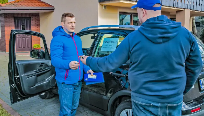 Mężczyzna w niebieskiej kurtce przekazuje kluczyki i dokumenty. Uczy się, jak negocjować cenę samochodu używanego.