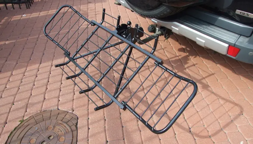 Czarny, metalowy uchwyt do przewozu motocykla na hak, gotowy do montażu przy samochodzie.