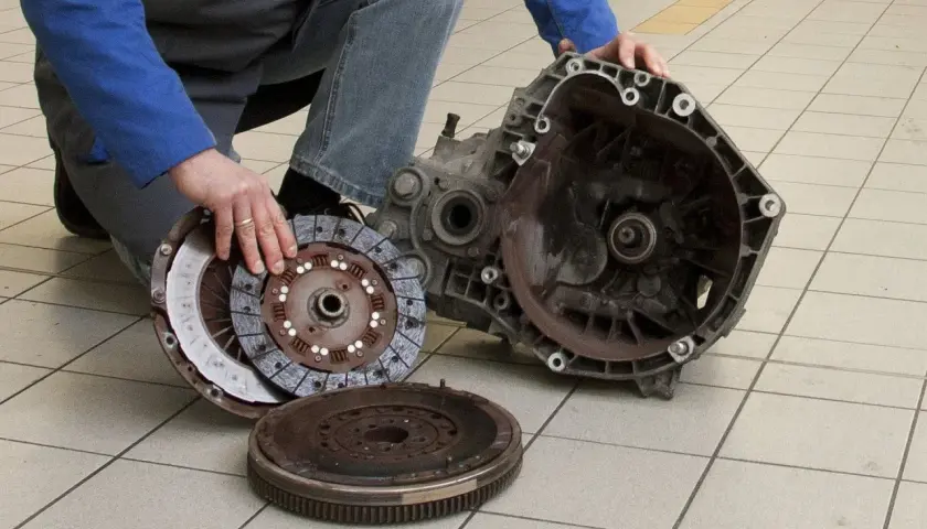 Mechanik pokazuje rozłożony element sprzęgła, w tym koło zamachowe i tarczę, gotowe do wymiany łożyska wałka sprzęgłowego.