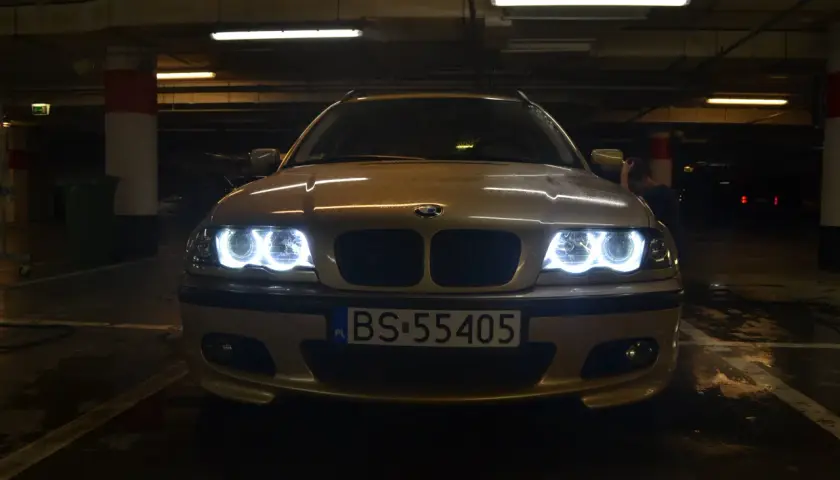 Złote BMW E46 z włączonymi ringami świeci w ciemnym garażu.