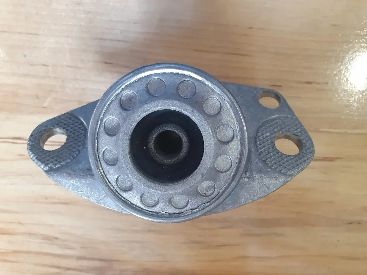 Metalowe górne mocowanie amortyzatora z gumowym elementem centrującym i otworami montażowymi.