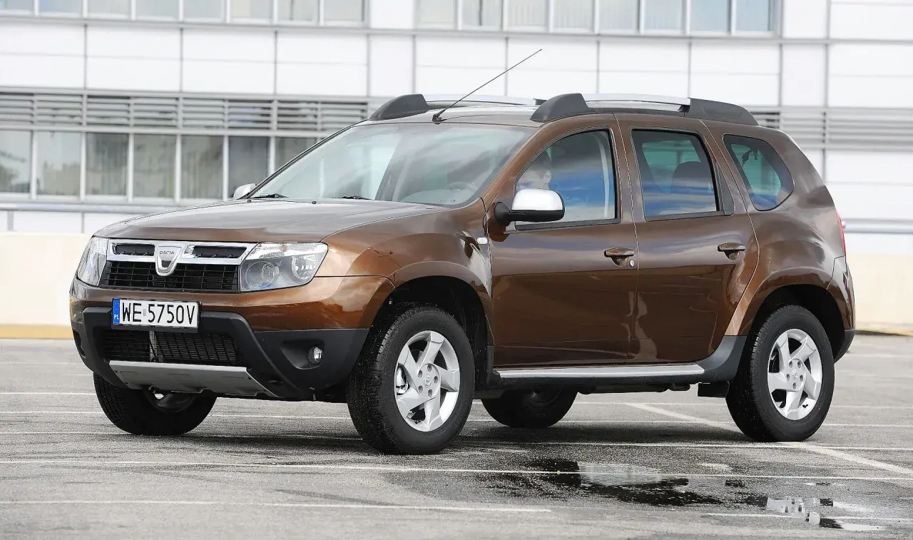 Brązowy Dacia Duster na parkingu. Zastanawiasz się, dacia duster jaki silnik wybrać? Ten model ma napęd 4x4.