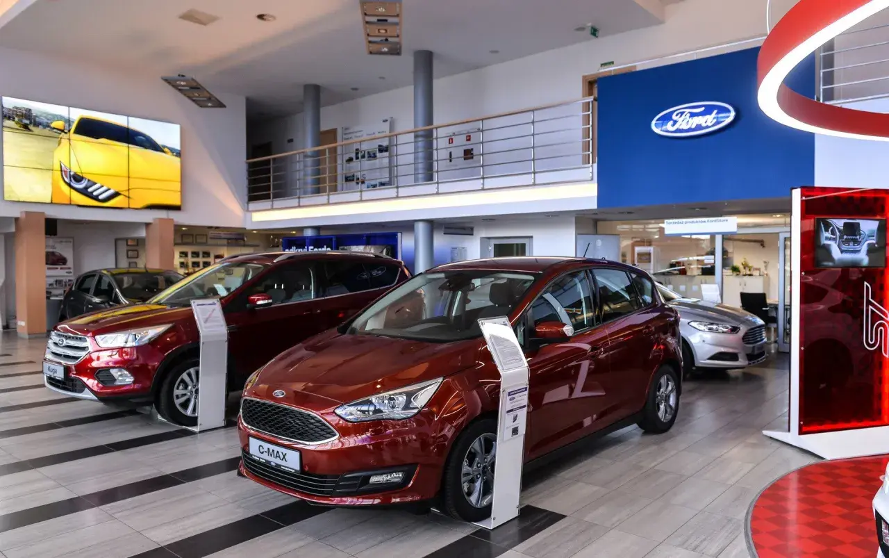 Salon Forda z czerwonym C-Maxem i Kuga na pierwszym planie. Zastanawiasz się, ile można negocjować cenę samochodu?