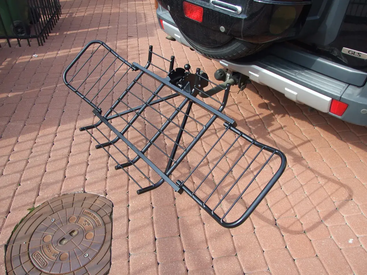 Czarny, metalowy uchwyt do przewozu motocykla na hak, gotowy do montażu przy samochodzie.