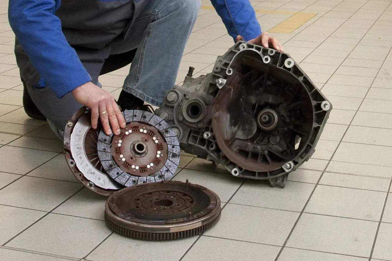 Mechanik pokazuje rozłożony element sprzęgła, w tym koło zamachowe i tarczę, gotowe do wymiany łożyska wałka sprzęgłowego.