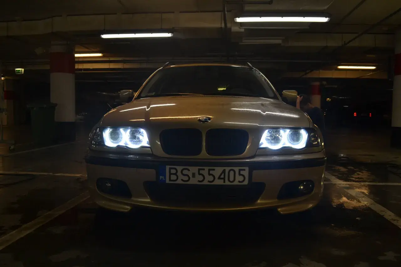 Złote BMW E46 z włączonymi ringami świeci w ciemnym garażu.
