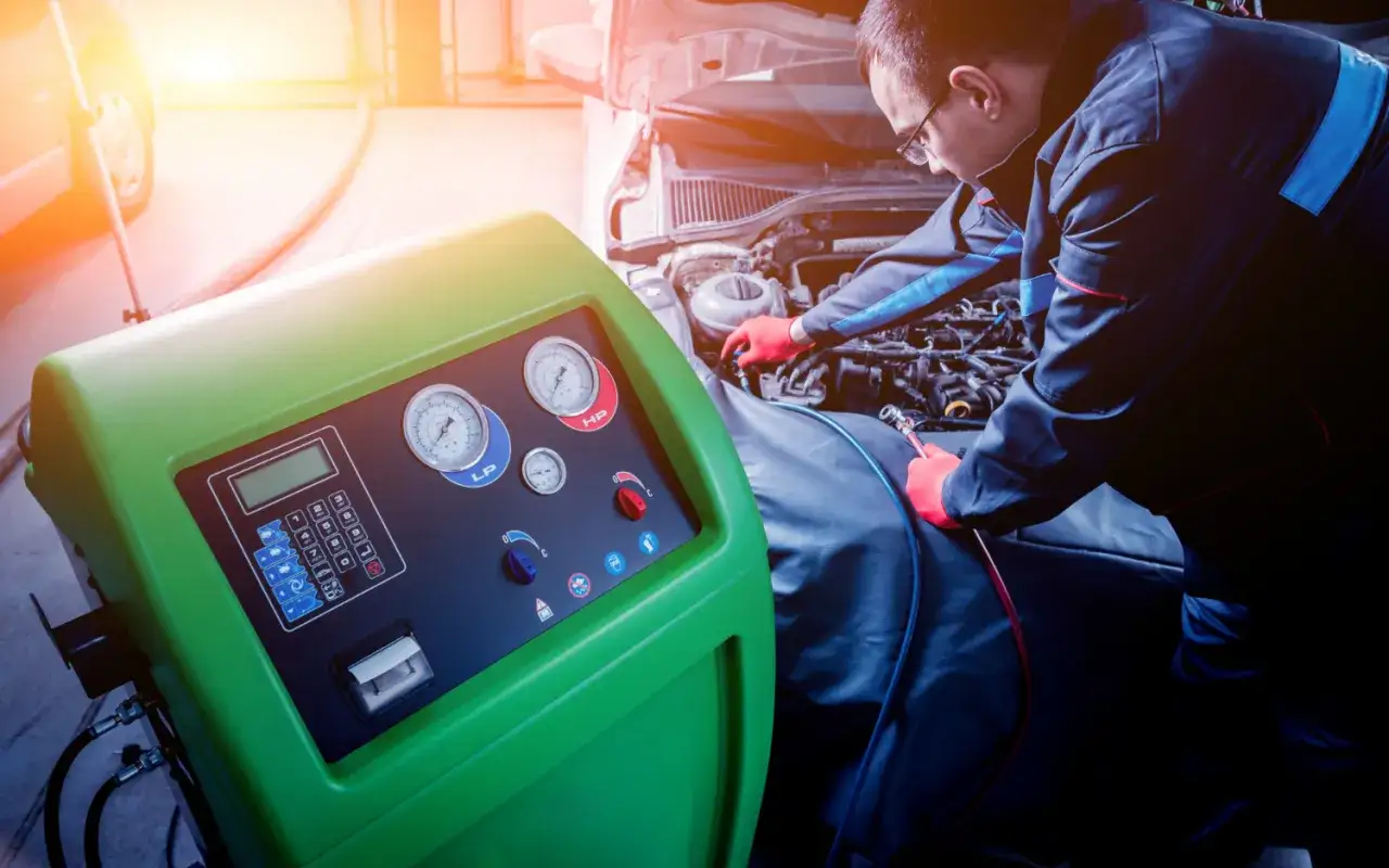 Mechanik naprawia klimatyzację samochodową, słychać syczenie z klimatyzacji. Urządzenie diagnostyczne z manometrami.