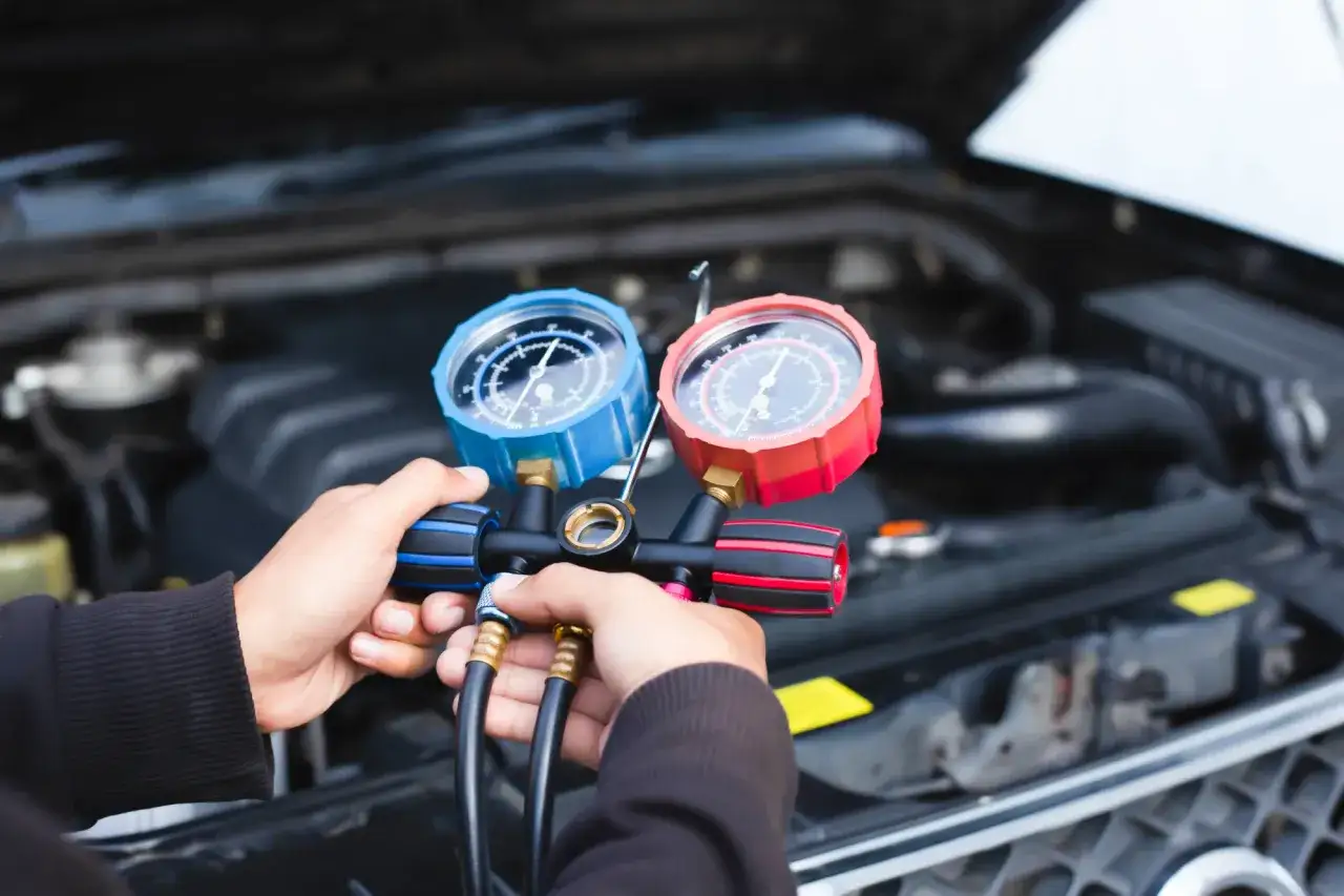 Mechanik dokonuje wymiany zaworu rozprężnego klimatyzacji, używając manometrów do kontroli ciśnienia w układzie.