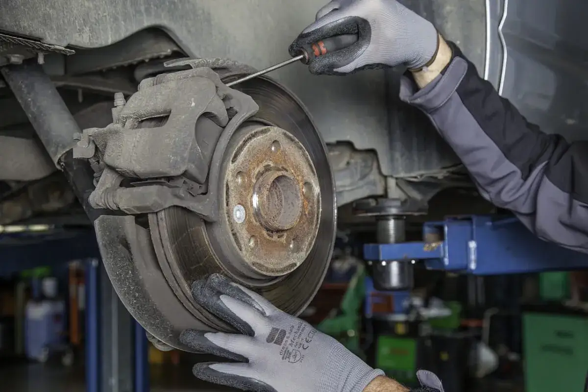 Mechanik w rękawiczkach sprawdza hamulce, by wyeliminować szuranie przy hamowaniu.