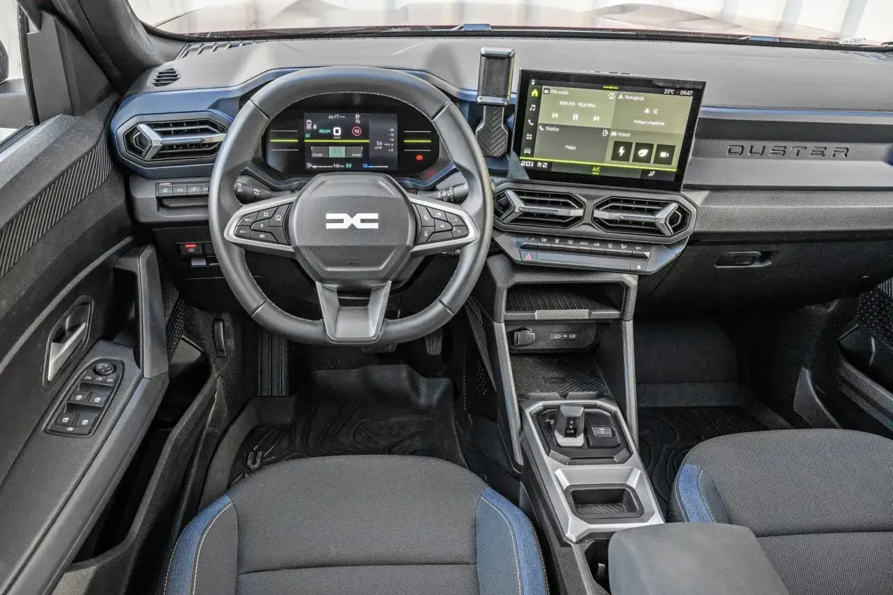 Wnętrze Dacia Duster: kierownica z przyciskami, cyfrowy ekran kierowcy, dotykowy ekran multimediów, dźwignia zmiany biegów i nawiewy.
