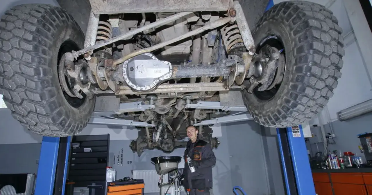 Mechanik przygotowuje się do wymiany oleju w dyferencjale terenowego samochodu, który uniesiony jest na podnośniku.