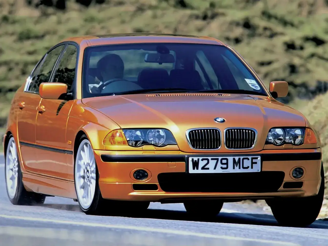 Pomarańczowe BMW E46, produkowane w latach 1997-2006, pędzi po drodze.