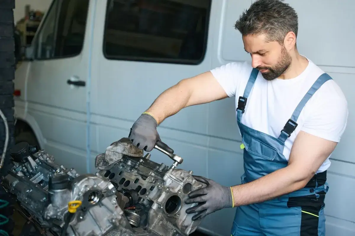 Mechanik w warsztacie naprawia silnik samochodu, używając klucza.