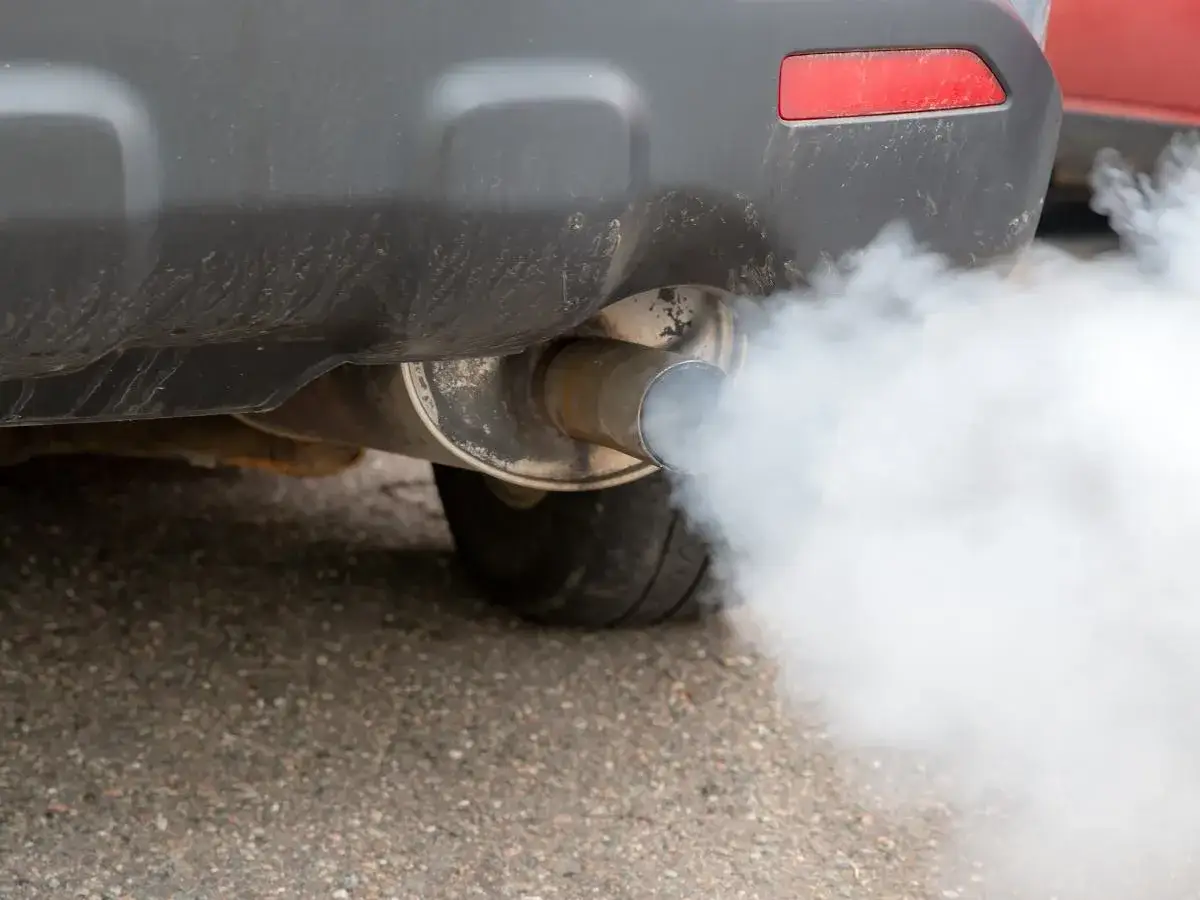Auto pluje wodą z wydechu, tworząc gęstą, białą chmurę pary. Widać fragment zderzaka i oponę.