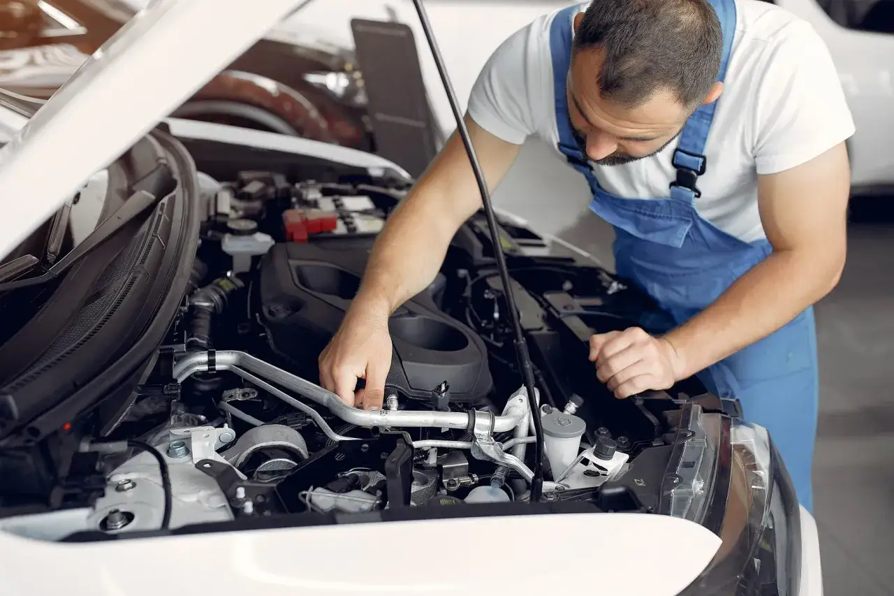 Mechanik w niebieskim kombinezonie sprawdza czujnik ciśnienia w kolektorze ssącym silnika samochodowego.