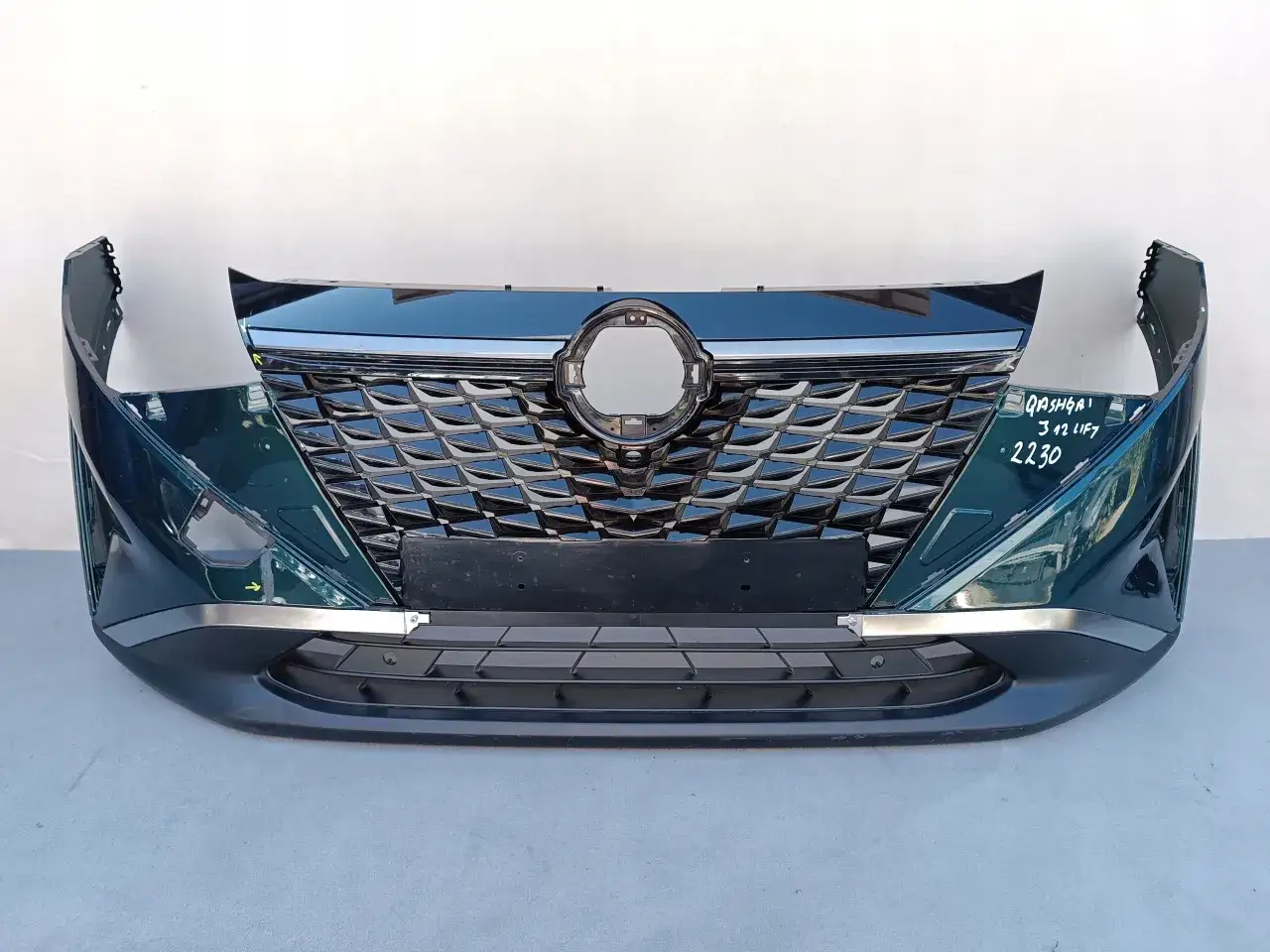 Zderzak Nissan Qashqai w kolorze ciemnozielonym, z charakterystycznym chromowanym grillem i srebrnymi wstawkami.