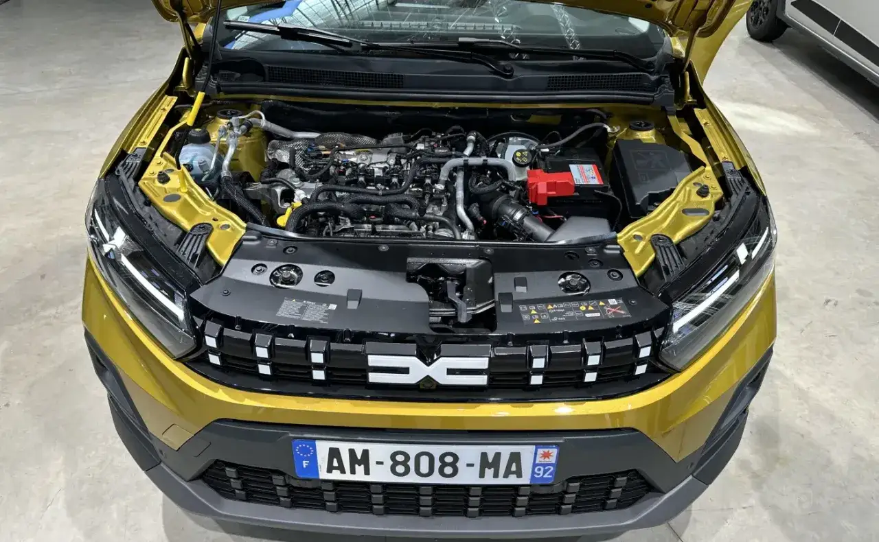 Złoty Dacia Sandero Stepway z otwartą maską, ukazującą silniki i ich skomplikowaną budowę.