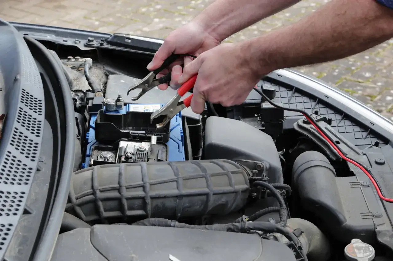 Ręce podłączają kable do akumulatora, próbując odpalić auto, które gaśnie.