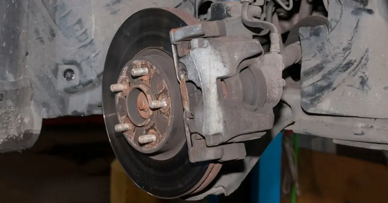 Widok z bliska na mechanizm hamulcowy samochodu, w tym na tarczę i zacisk. Widać, że gorące tarcze hamulcowe z tyłu wymagają uwagi.