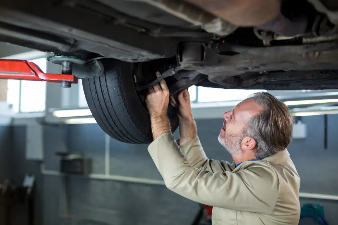 Mechanik pracuje pod podniesionym samochodem, montując zestaw naprawczy amortyzatora.