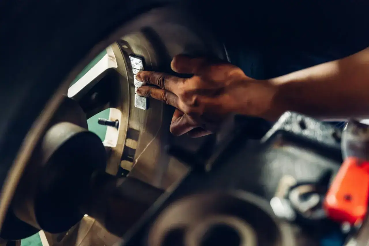 Mechanik przykleja ciężarki do felgi, aby wyeliminować wibracje podczas przyspieszania.